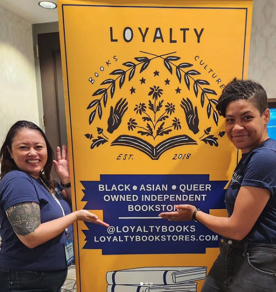 Loyalty co-owners, Hannah Oliver Depp and Christine Bollow, pose in front of a Loyalty Bookstore banner.